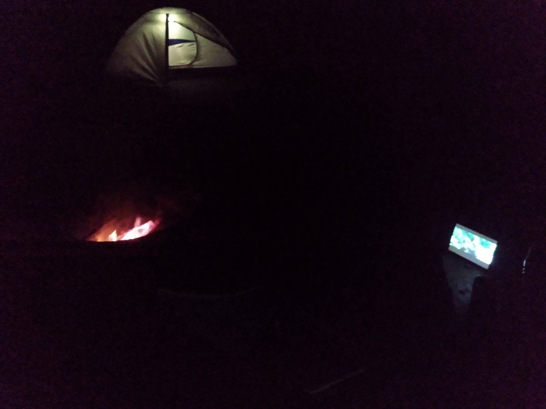 campfire, tent and tablet screen at night